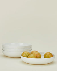 Three Simple Porcelain Low Bowls - Set of 4 by Hawkins New York are shown, with one bowl filled with passion fruits, all against a plain background. Bring the elegance of Hawkins New York porcelain dinnerware into your home.