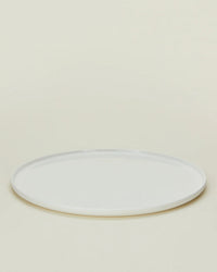 A Simple Porcelain Salad Plate from Hawkins New Yorks set of 4 is displayed empty on a light beige background, viewed from a slight angle. The plain, round white plate evokes fine dinnerware style.