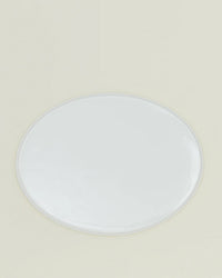 The Simple Porcelain Serving Platter by Hawkins New York, an oval white dish with a glossy finish, sits centered on a light beige background, showcasing the refined elegance of porcelain dinnerware.