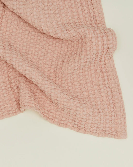 A close-up of the Simple Waffle Bath Sheet in Blush by Hawkins New York, featuring a soft, textured waffle-knit pattern and neatly folded on a light cream-colored surface.