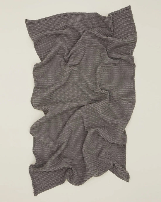 The Simple Waffle Bath Sheet in Dark Grey by Hawkins New York, inspired by luxurious Portuguese towels, is shown spread on a light surface with soft folds and textured waffle-knit detail.