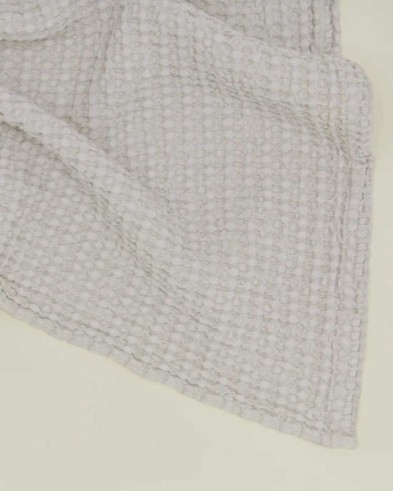 A close-up of the Hawkins New York Simple Waffle Bath Sheet in Light Grey, showcasing its Portuguese-made waffle weave texture, partially folded on a light surface.