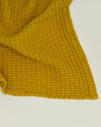 A close-up of the Simple Waffle Bath Sheet in Mustard by Hawkins New York, featuring a textured waffle weave pattern, is laid flat on a light surface.