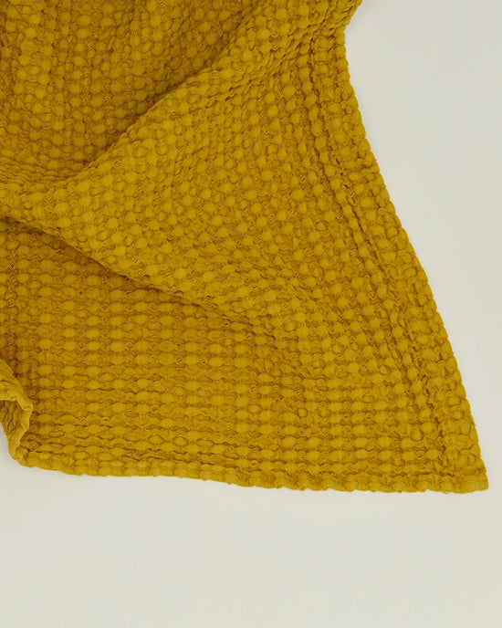 A close-up of the Simple Waffle Bath Sheet in Mustard by Hawkins New York, featuring a textured waffle weave pattern, is laid flat on a light surface.