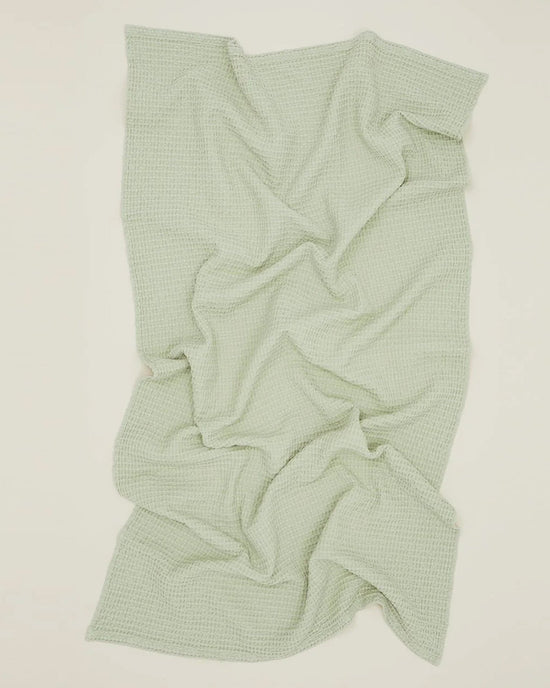 The Hawkins New York Simple Waffle Bath Sheet in Sage, featuring a textured waffle-knit reminiscent of luxury towels, is spread out on a light surface with gentle folds and creases.