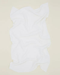 The Hawkins New York Simple Waffle Bath Sheet in White is laid flat on a light beige surface, its soft folds and wavy edges highlighting the high quality of this absorbent cotton towel.