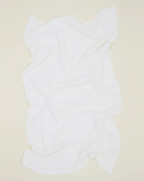 The Hawkins New York Simple Waffle Bath Sheet in White is laid flat on a light beige surface, its soft folds and wavy edges highlighting the high quality of this absorbent cotton towel.