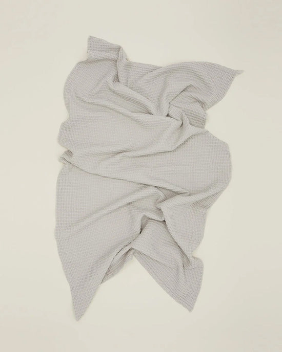 The Simple Waffle Bath Towel in Light Grey by Hawkins New York is spread out on a plain off-white background, showcasing its textured, stonewashed cotton finish.