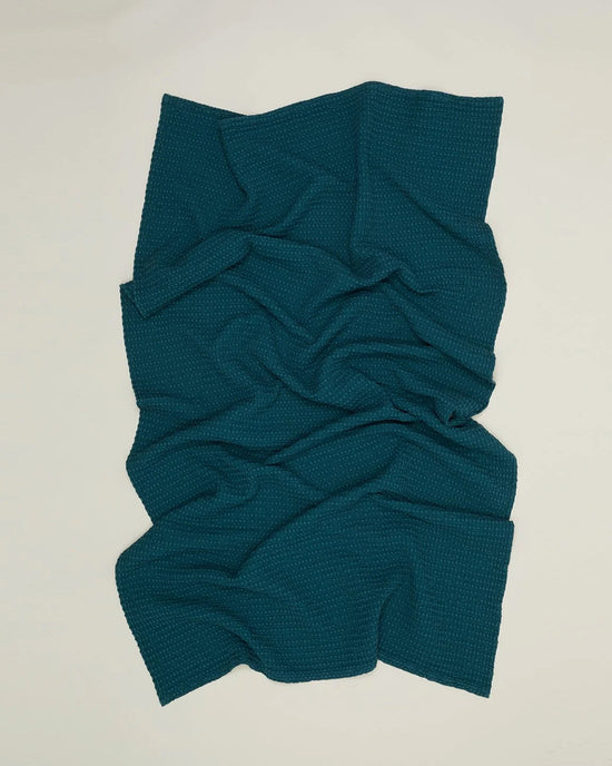 The Simple Waffle Bath Towel in Peacock by Hawkins New York is laid flat on a light surface, showing natural folds and wrinkles that create a wavy look.