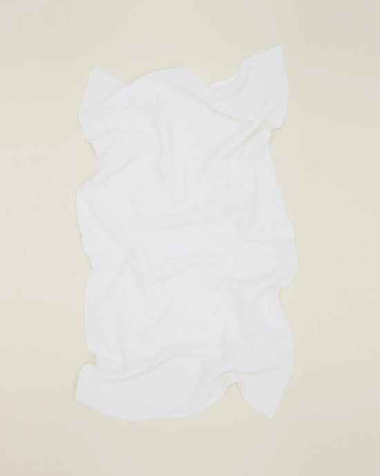The Hawkins New York Simple Waffle Bath Towel in White lies flat on a pale beige surface, featuring a soft texture, wavy edges, and visible folds that highlight its slightly irregular shape.