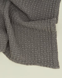 A close-up of the Hawkins New York Simple Waffle Hand Towel in Dark Grey highlights its textured, bumpy weave and a neatly folded corner.