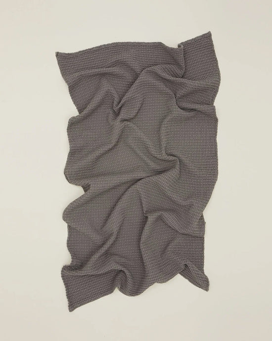 The Hawkins New York Simple Waffle Hand Towel in Dark Grey is laid flat on a light surface, displaying its textured waffle weave with soft folds and wrinkles.