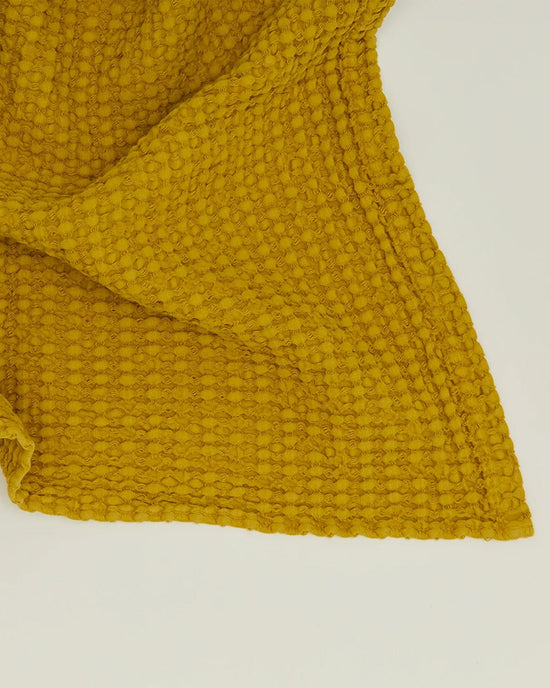 The Simple Waffle Hand Towel in Mustard by Hawkins New York, featuring a textured waffle-like pattern, is displayed on a plain white surface.