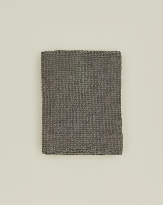 The Simple Waffle Shower Curtain in Dark Grey by Hawkins New York is displayed neatly folded on a plain light-colored surface.