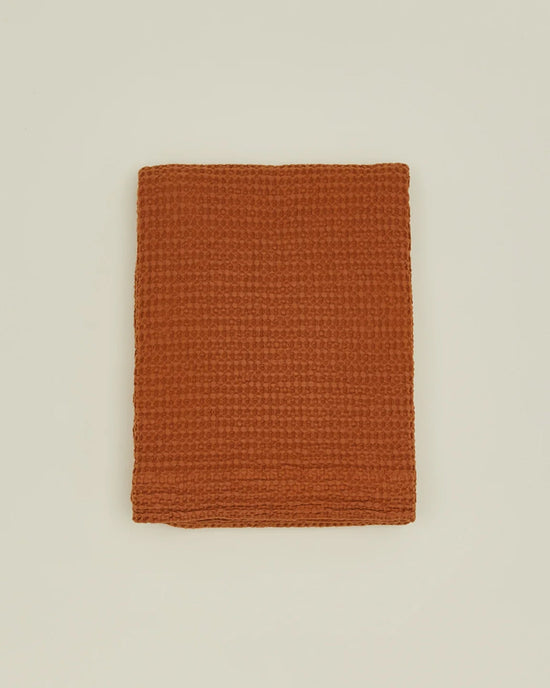 A folded, textured terracotta towel is set on a plain off-white background, evoking the warm tones of the Hawkins New York Simple Waffle Shower Curtain in Terracotta.