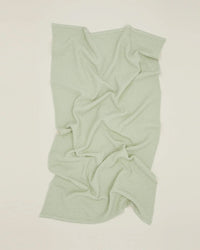 The Simple Waffle Washcloth in Sage by Hawkins New York, featuring a textured waffle weave, is displayed flat on an off-white surface with visible folds and creases.