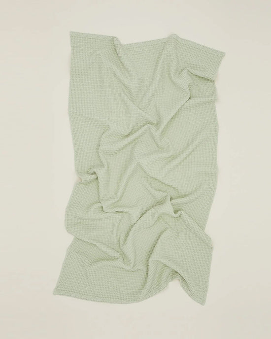 The Simple Waffle Washcloth in Sage by Hawkins New York, featuring a textured waffle weave, is displayed flat on an off-white surface with visible folds and creases.