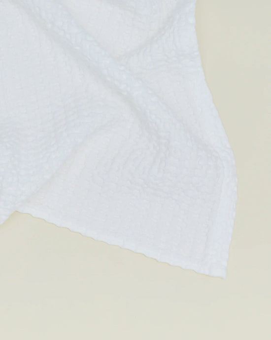 A close-up of the Simple Waffle Washcloth in White by Hawkins New York, featuring a textured waffle pattern and expertly crafted in Portugal, partially draped on a light-colored surface.