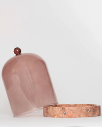 The Poured New York Cloche + Stone in Nude features a translucent, brown-tinted glass cover with a knob paired with a round marble base—an elegant candle accessory displayed against a plain white background.