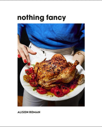 A person in a blue shirt holds a platter of roasted chicken and tomatoes. The cover text reads Nothing Fancy by Random House, highlighting the approachable style of this cookbook filled with easy entertaining recipes.