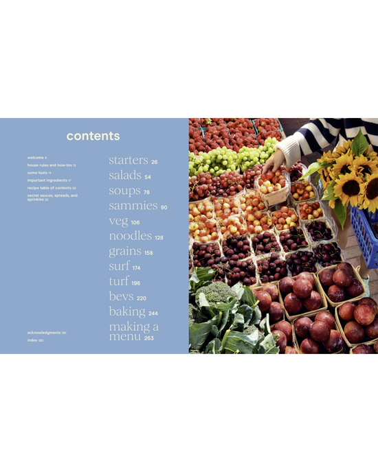 At a bustling market stall with fresh produce like tomatoes, plums, and greens, someone holds yellow fruits—great inspiration for recipes from The Wishbone Kitchen Cookbook by Random House.