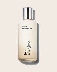 A frosted bottle with a silver cap labeled Dulce Everyday Body Milk by Rosie Jane sits against a light beige background.
