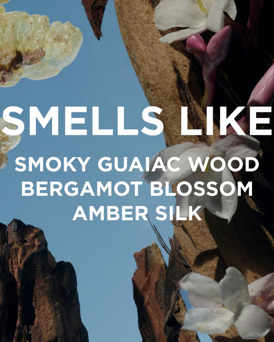 Bright blue sky with white/pink flowers, brown rocks, and crystals. Bold white text: Smells like smoky guaiac wood, bergamot blossom, amber silk—Rosie Jane Perfume Oil in Dylan (unisex).