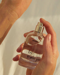 A hand holds a clear glass bottle of Eau De Parfume in James by Rosie Jane as a finger presses the spray nozzle.