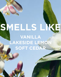 Close-up of blooming flowers and green leaves against a blue sky. Overlaid text reads: SMELLS LIKE Vanilla Lakeside Lemon Soft Cedar—recalling Rosie Jane Perfume Oil in Lake’s concentrated fragrance.