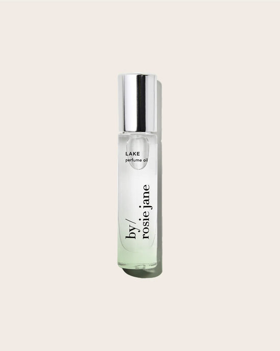 The Rosie Jane Perfume Oil in Lake, shown in a clear glass bottle with a silver cap against a light beige background, offers a concentrated fragrance that captures the essence of nature.