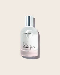 The Eau De Parfume in Leila Lou by Rosie Jane, in a clear glass bottle with a silver cap, is elegantly displayed against a light beige background—a signature floral scent.