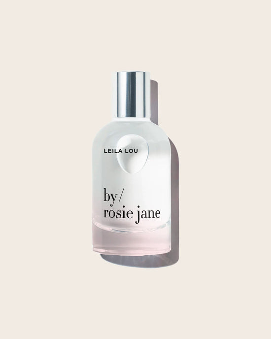 The Eau De Parfume in Leila Lou by Rosie Jane, in a clear glass bottle with a silver cap, is elegantly displayed against a light beige background—a signature floral scent.
