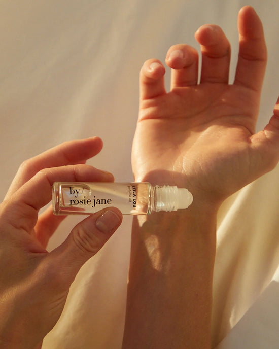A hand applies Rosie Jane’s Perfume Oil in Leila Lou to another’s wrist, as soft sunlight highlights the gesture and evokes a delicate floral scent.