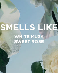 Close-up of dewy white roses against a blue sky, with bold text: SMELLS LIKE WHITE MUSK SWEET ROSE. Featuring Rosie Jane’s Rosie Everyday Body Oil to hydrate skin and leave you softly scented.
