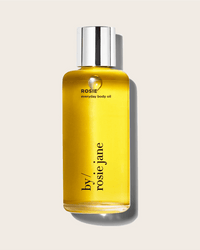 A clear bottle of yellow Rosie Everyday Body Oil by Rosie Jane with a silver cap is shown against a light beige background. This hydrating oil is ideal for daily use.