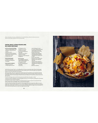 An open Mussels cookbook by Simon & Schuster features a recipe on the left and a vivid photo of stew or curry garnished with herbs and crispy bread on the right, set against a dark cloth backdrop—ideal for mussel recipes.