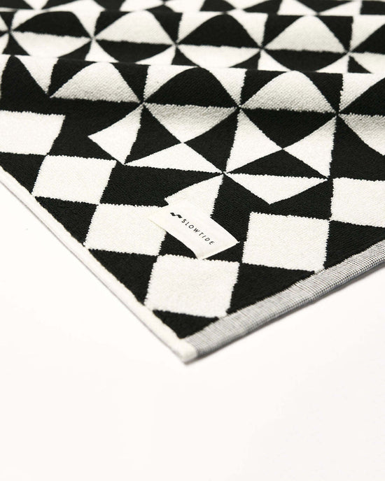 The Slowtide Gatsby Bath Mat in Black, made from sustainable cotton, showcases a geometric triangle design and a visible fabric tag, displayed on a white background.