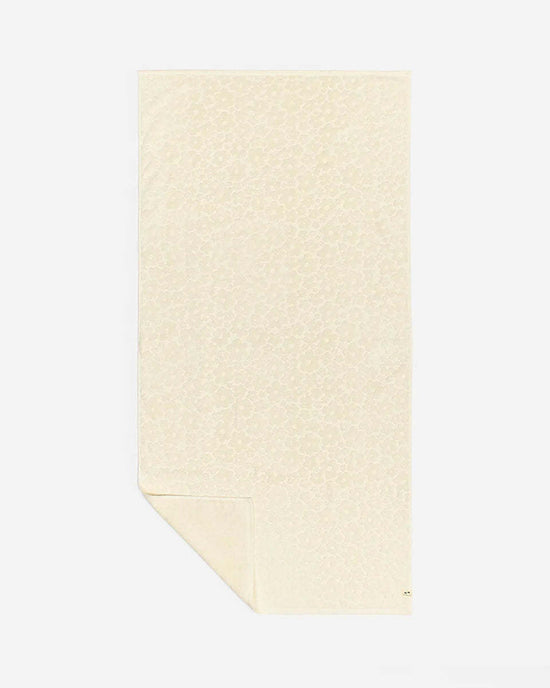 The Ginny Bath Towel by Slowtide is a beige, rectangular towel made from sustainably sourced cotton with a subtle animal print. Shown flat with a folded corner, it adds spa-like comfort and elegance to your bath routine.