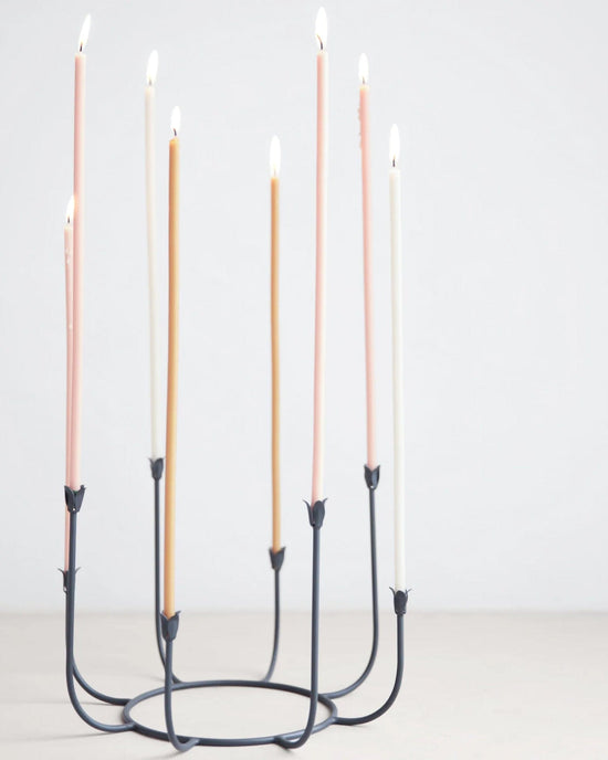 The Floral Society’s Beacon Long Stem Candelabra in Smoke, featuring eight lit pastel taper candles, is showcased against a plain light background.