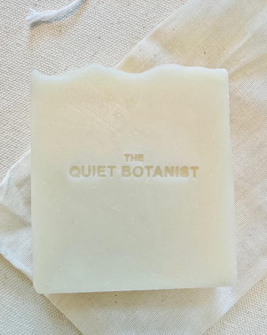 The Quiet Botanists Everyday - Handmade Soap is a white rectangular olive oil bar, embossed with the brand name and crafted for sensitive skin, featuring a subtle natural fragrance. Shown on a light fabric surface.