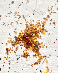 A scattered pile of dried chili flakes and seeds on a white textured surface, perfect for adding a spicy kick to The Quiet Botanist’s caffeine-free Love Poem Tea.