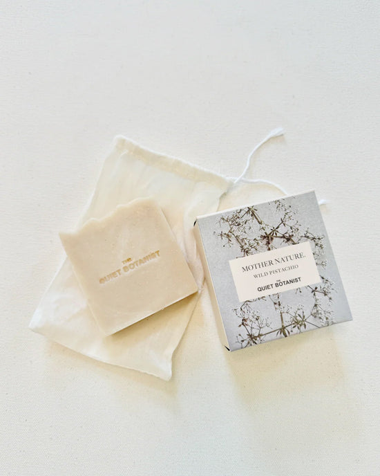 A bar of The Quiet Botanists Mother Nature - Handmade Soap rests on a cloth pouch beside its botanical-themed box, offering gentle cleansing and deep hydration.