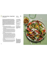 A vibrant plate from The Salad Project by Random House—steak, sweet potato, arugula, cheese, tomatoes, and crispy onions—rests beside a glass of water and finished bowl. Salad recipes appear in the open cookbook on the left.