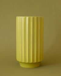 The Monroe Vase in Palm by Jungle Club is a tall, cylindrical ceramic vase with a ribbed design, shown against a matching yellow background for a chic, monochromatic style perfect for floral lovers.