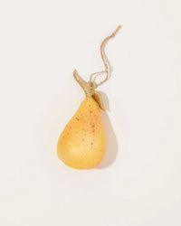 The Cody Foster Orchard Pear in Speckle Sparkle ornament, yellow with red speckles and a gold glitter leaf, hangs from twine against a plain white background.