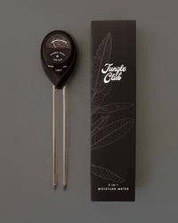 The Jungle Club 3-in-1 Moisture Meter in Black, with two metal probes, is shown beside its black box featuring leaf designs and the white Jungle Club logo—an ideal tool for monitoring plant health.