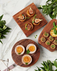 The etúHOME New Classic Round Trivet Riser, Small, highlights assorted pastries—fig tarts, orange slices, and herbs—on a marble surface with greenery and cutlery. A must-have serving essential for your kitchen.