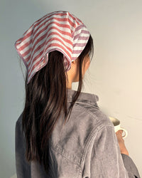 A woman with a towel on her head thoughtfully admires the Casa Amarosa Stripe Hand Block Printed Scarf in Purple & Red, imagining how it would enhance her style.