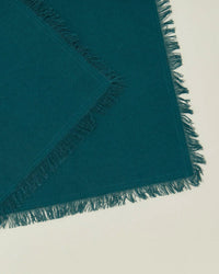 A set of four Essential Cocktail Napkins in Peacock by Hawkins New York, made from 100% cotton with fringed edges, are displayed on a light off-white background.