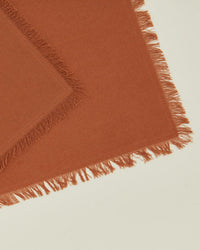 The Essential Cocktail Napkins in Terracotta by Hawkins New York are 100% cotton with fringed edges and a tasseled border, shown overlapping at an angle for a chic display. Set of 4.